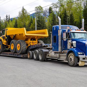 Big truck with a low platform trailer carrying a tipper truck on a public parking area of a truck stop